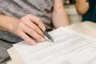 mano está apoyada con un boli sobre un contrato, la actituad del usuario es de leer el documento